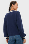 A woman models the Washed Navy Ashe Sweater with balloon sleeves and a contrast V-neckline, showcasing classic, effortless style in a high-end, fun knit design.