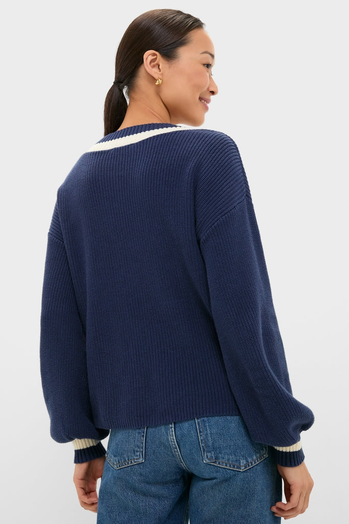 A woman models the Washed Navy Ashe Sweater with balloon sleeves and a contrast V-neckline, showcasing classic, effortless style in a high-end, fun knit design.