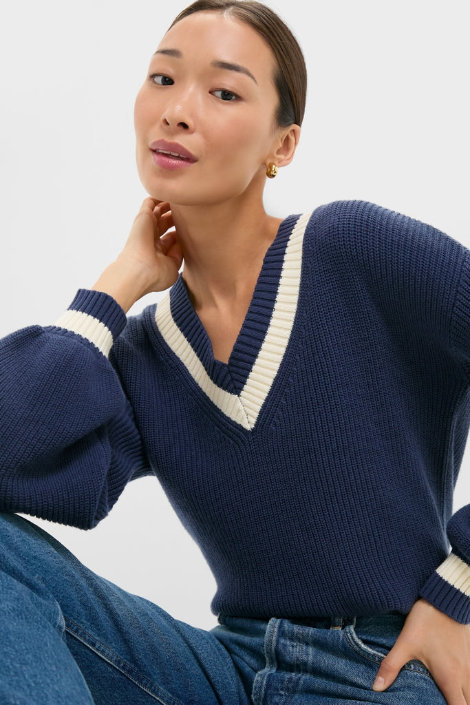 Young woman wearing the Washed Navy Ashe Sweater with a deep V-neck and off-white stripes, effortlessly styled with balloon sleeves for a classic, high-end look.