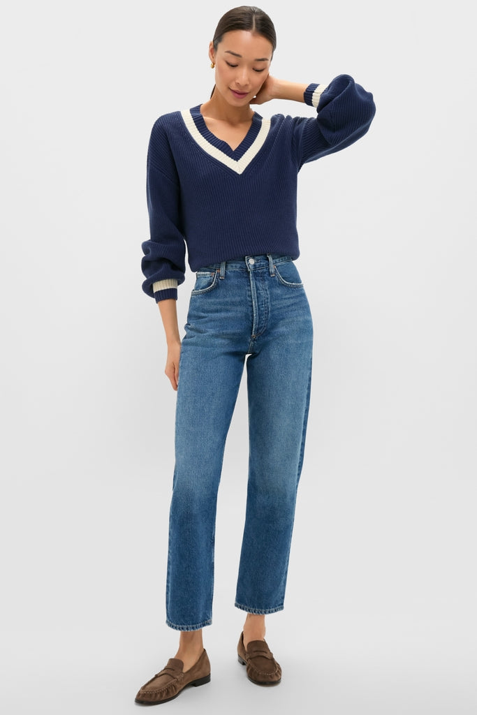 Woman models the classic Washed Navy Ashe Sweater with a deep V-neck, balloon sleeves, and high-end ribbed cuffs, paired effortlessly with high-waisted jeans and loafers.
