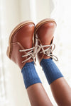 Classic Dark Tan Leather Kids Desert Boots in buttery-soft Nappa leather with self-tie laces, paired effortlessly with ribbed blue crew socks, embodying fun and high-end style.