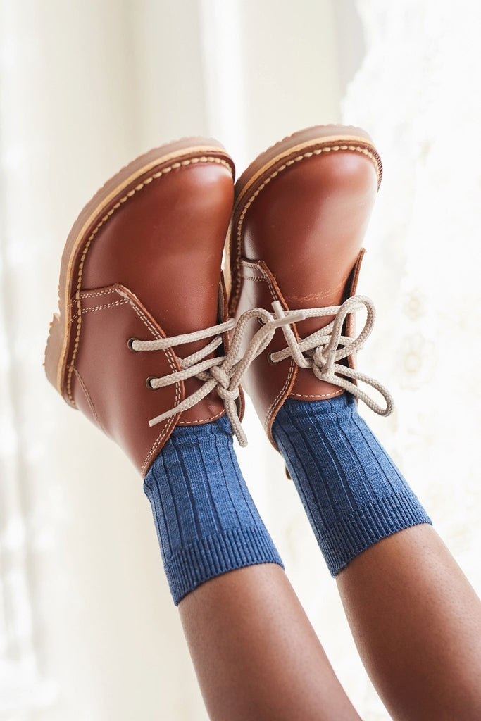 Classic Dark Tan Leather Kids Desert Boots in buttery-soft Nappa leather with self-tie laces, paired effortlessly with ribbed blue crew socks, embodying fun and high-end style.
