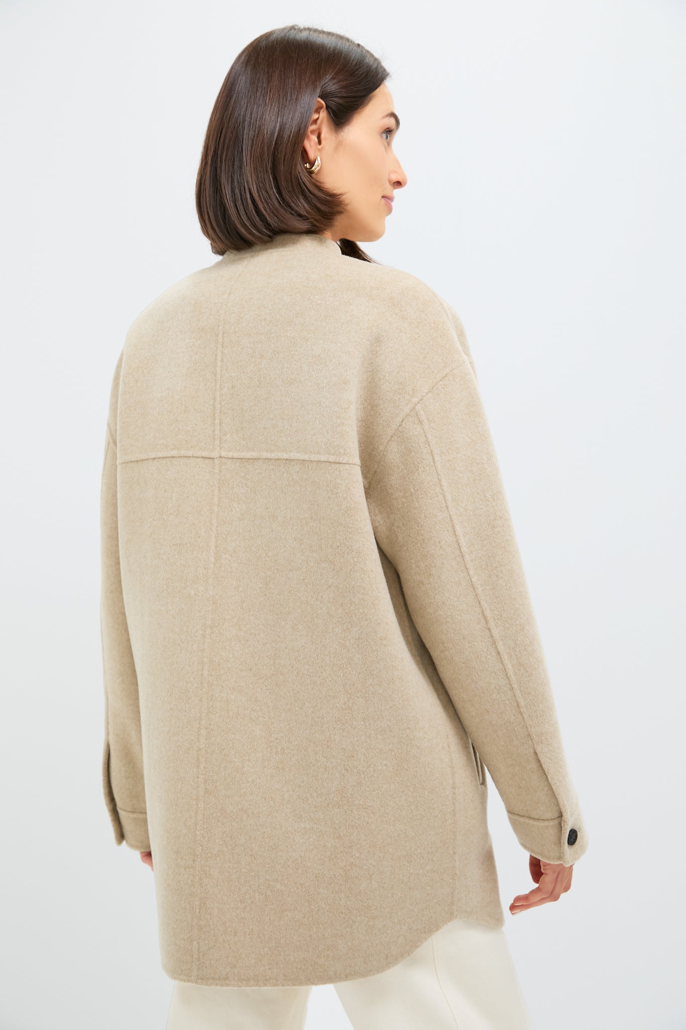 Back view of a woman in a classic, oversized Beige Chine Florian Coat with seam detailing, button cuffs, styled effortlessly with light trousers for a high-end, fun look.