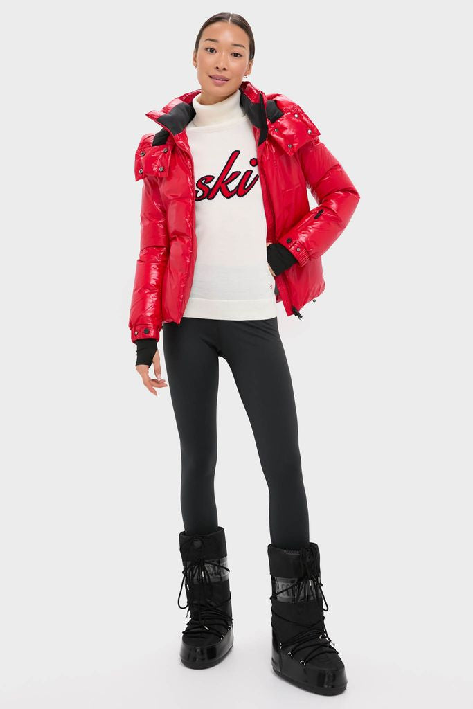 Woman in shiny red puffer jacket and ski sweater models classic, high-end Black Icon Glance Boots with effortless style, embodying fun and innovative ski fashion.