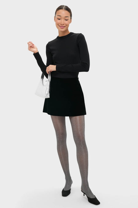 Model showcasing the Silver Mini Candy Bag, a classic, high-end metallic handbag with a circular strap, effortlessly complementing her chic black outfit and sparkly tights.