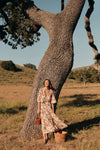Woman standing in front of a tree in a floral maxi dress. 