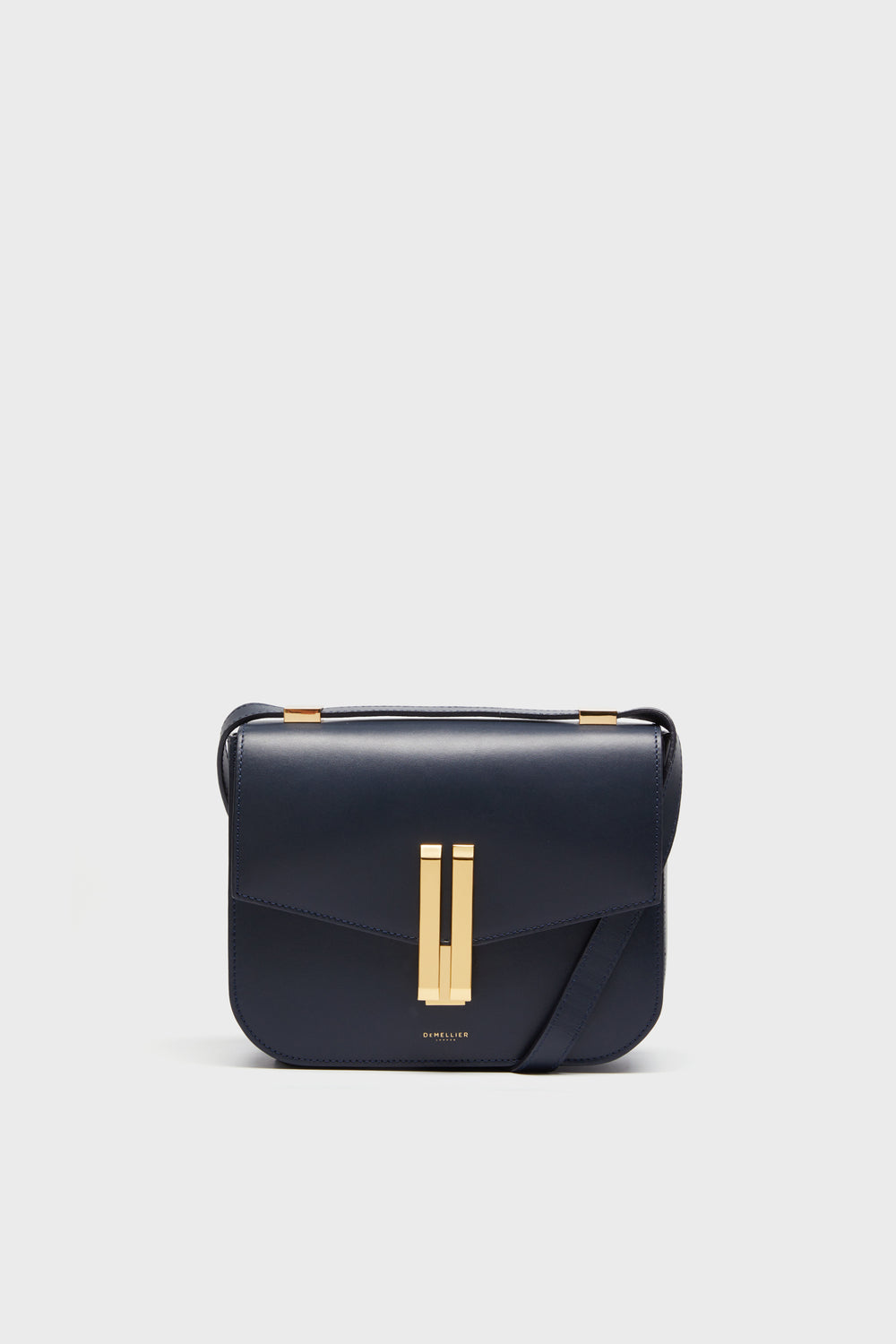 A navy blue handcrafted leather crossbody bag with a structured shape, flap closure, and gold-tone hardware by Demellier.