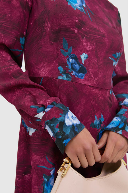 Woman wearing the Abstract Rose Milberry Red Long Sleeve Midi Dress, featuring blue floral motifs, holding a cream leather handbag. A classic, effortless, high-end style for any occasion.