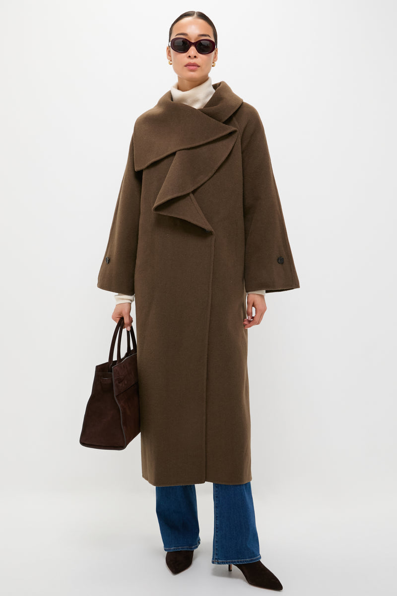 A person in a STAUD Taupe Noah Coat—a chic wool blend—paired with blue jeans, pointed brown shoes, sunglasses, and a brown handbag stands against a plain white background.