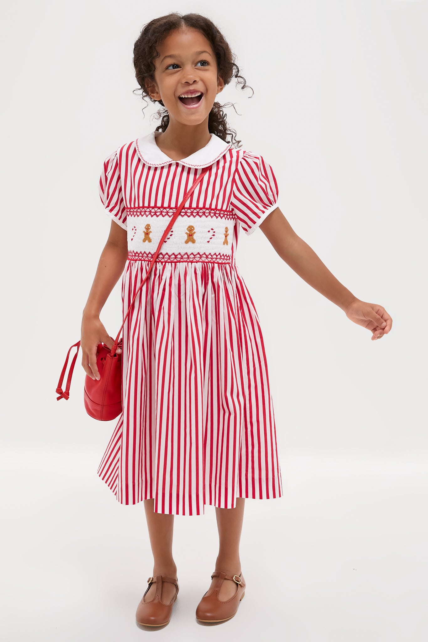 Young girl in a classic Candy Cane Stripe Smocked Dress with gingerbread embroidery, exuding an effortless, fun, and high-end holiday charm.