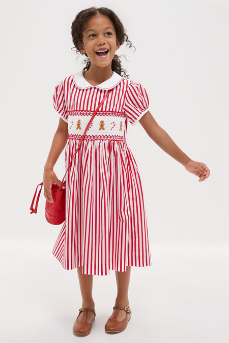 Young girl in a classic Candy Cane Stripe Smocked Dress with gingerbread embroidery, exuding an effortless, fun, and high-end holiday charm.