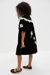 A young girl stands sideways in a Sea New York velveteen lace applique dress with white embroidered details, paired with leopard print flat shoes.