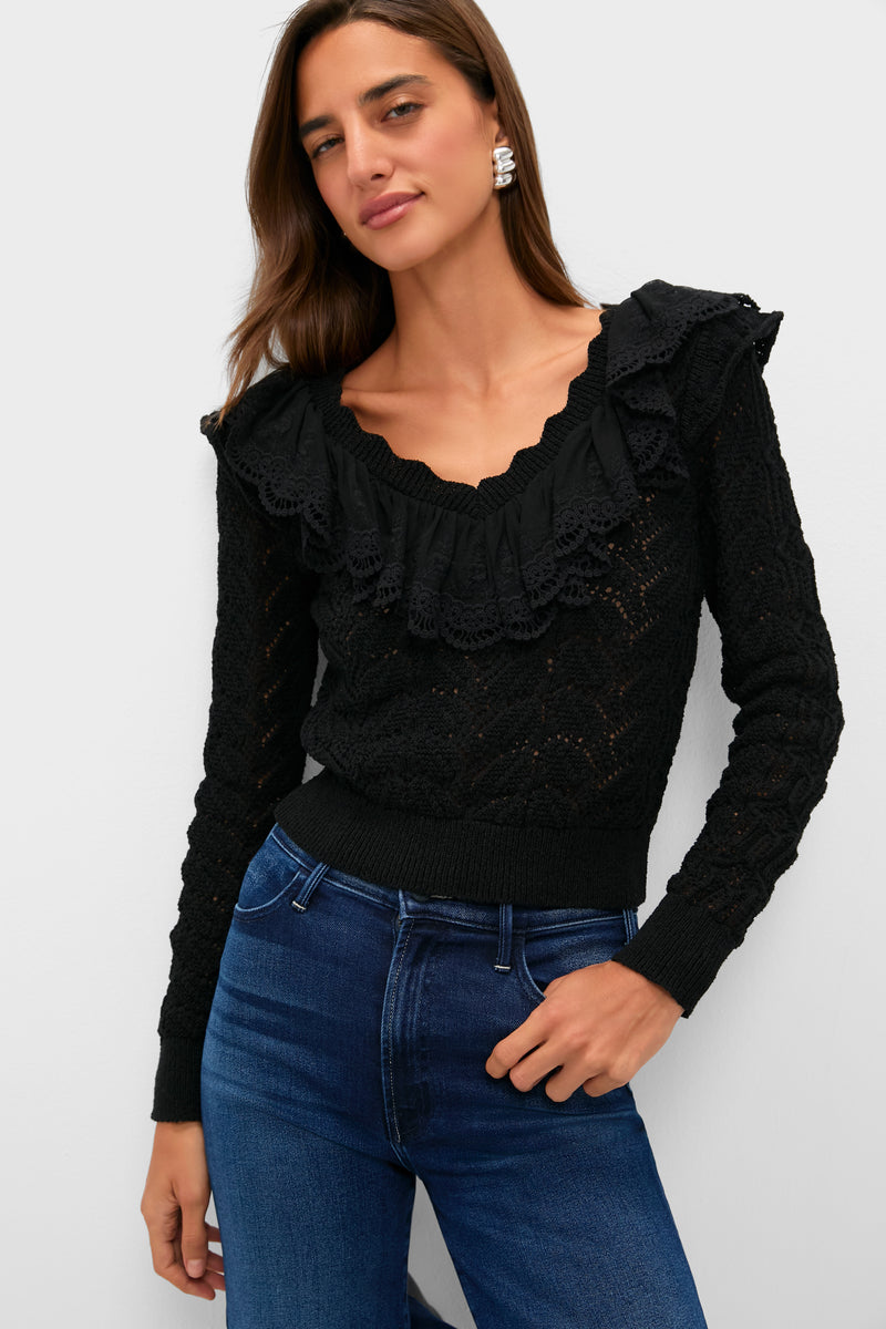 A woman stands confidently in a Hyacinth House black ruffled V-neck sweater with lace details, paired with blue jeans.