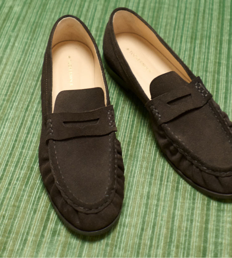 Brown suede loafers on a green background. 