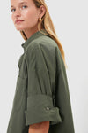 Woman in olive-green Duffle Bag Next Ex Shirt, featuring a boxy, cropped silhouette with rolled cuffs, embodying a classic yet effortless, high-end style.