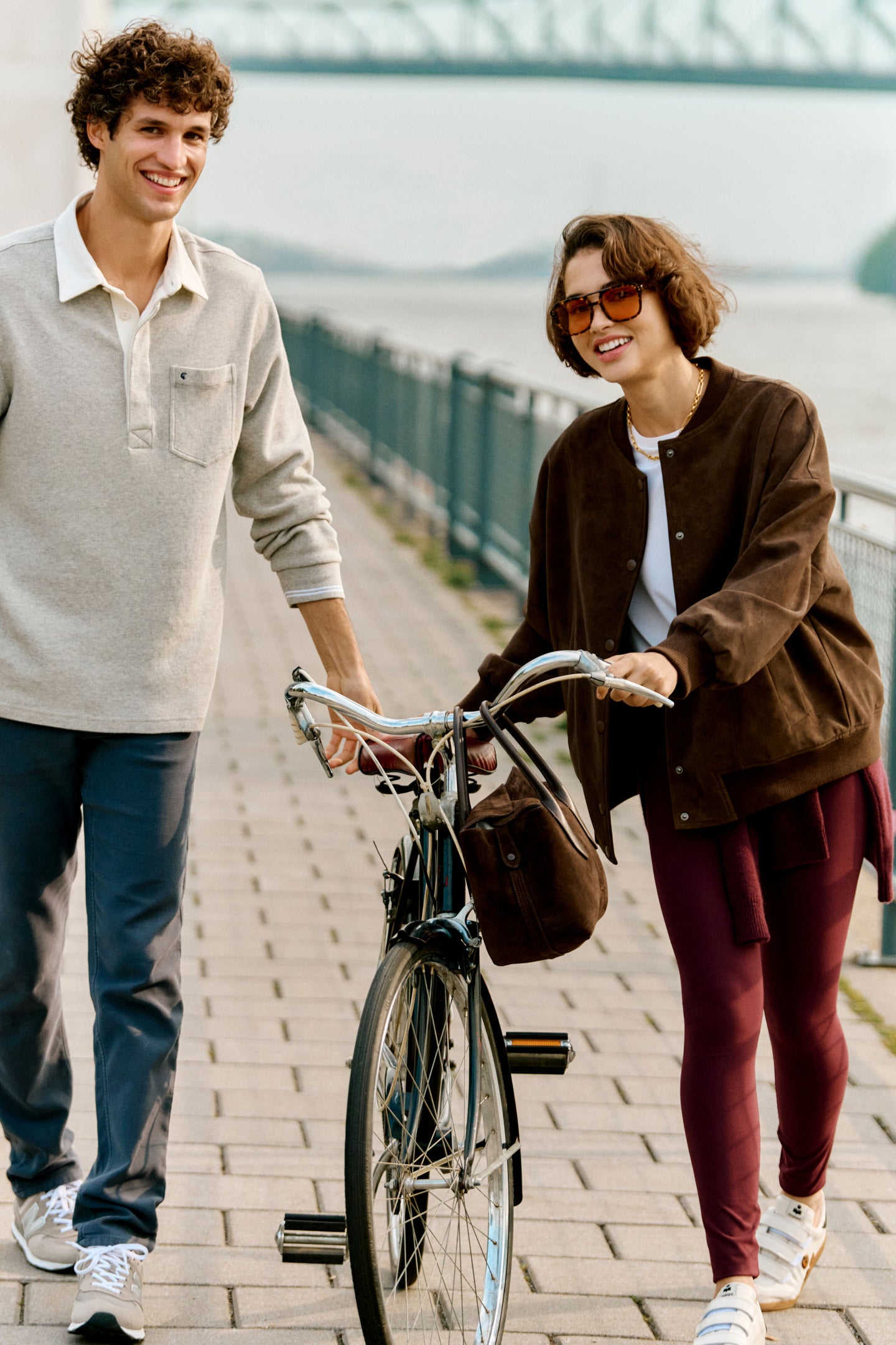 Young woman effortlessly strolling riverside in Chocolate Alfie Jacket, a classic faux leather piece, exuding high-end style and fun sophistication.