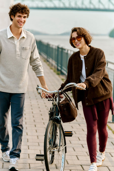 Young woman effortlessly strolling riverside in Chocolate Alfie Jacket, a classic faux leather piece, exuding high-end style and fun sophistication.