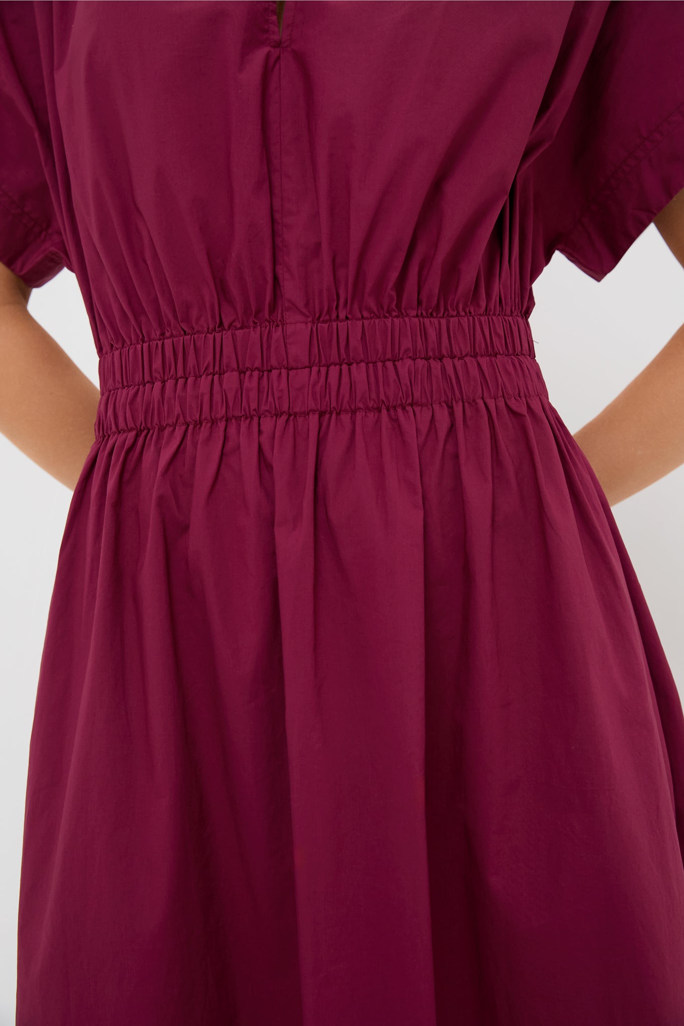 Close-up of a person in the Pomander Place Emmy Dress, a short-sleeve burgundy design with a smocked waist and hands at sides, showcasing its classic fit & flare silhouette.