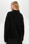 Person wearing Black Genevieve Cashmere Wool Blend Crewneck Sweater with ribbed hem, showcasing its classic, effortless, and high-end style, paired with black pants and a silver earring.