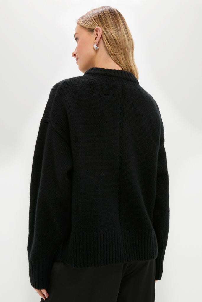 Person wearing Black Genevieve Cashmere Wool Blend Crewneck Sweater with ribbed hem, showcasing its classic, effortless, and high-end style, paired with black pants and a silver earring.