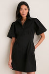 Woman in Black Mini Delaney Dress with puff sleeves and pleated waist, exuding a classic, effortless style perfect for high-end, fun occasions.