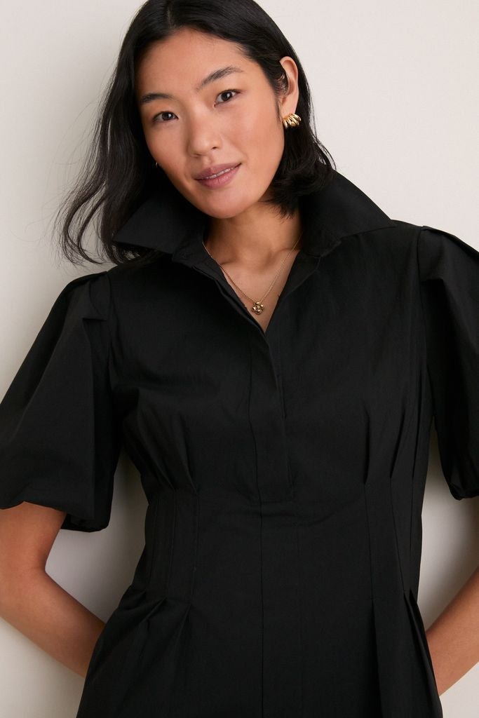 Woman wearing the Black Mini Delaney Dress with a spread collar and puff sleeves, accessorized with gold jewelry, embodying a classic, effortless, and high-end look.