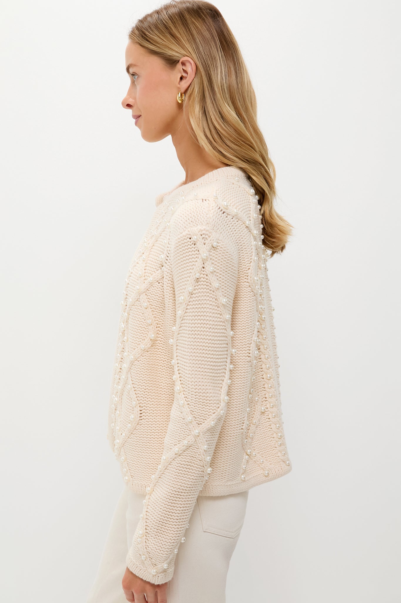 Woman wearing Cream Cable Knit Pearl Collins Cardigan with pearl embellishments, showcasing an effortless, high-end look, embodying classic style and fun elegance.