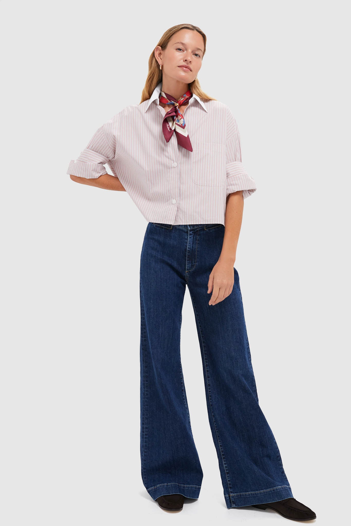 Model wearing the Spanish Villa and White Next Ex Shirt, a classic, cropped button-down with pink-and-white stripes and rolled sleeves, paired with high-waisted, wide-leg jeans.
