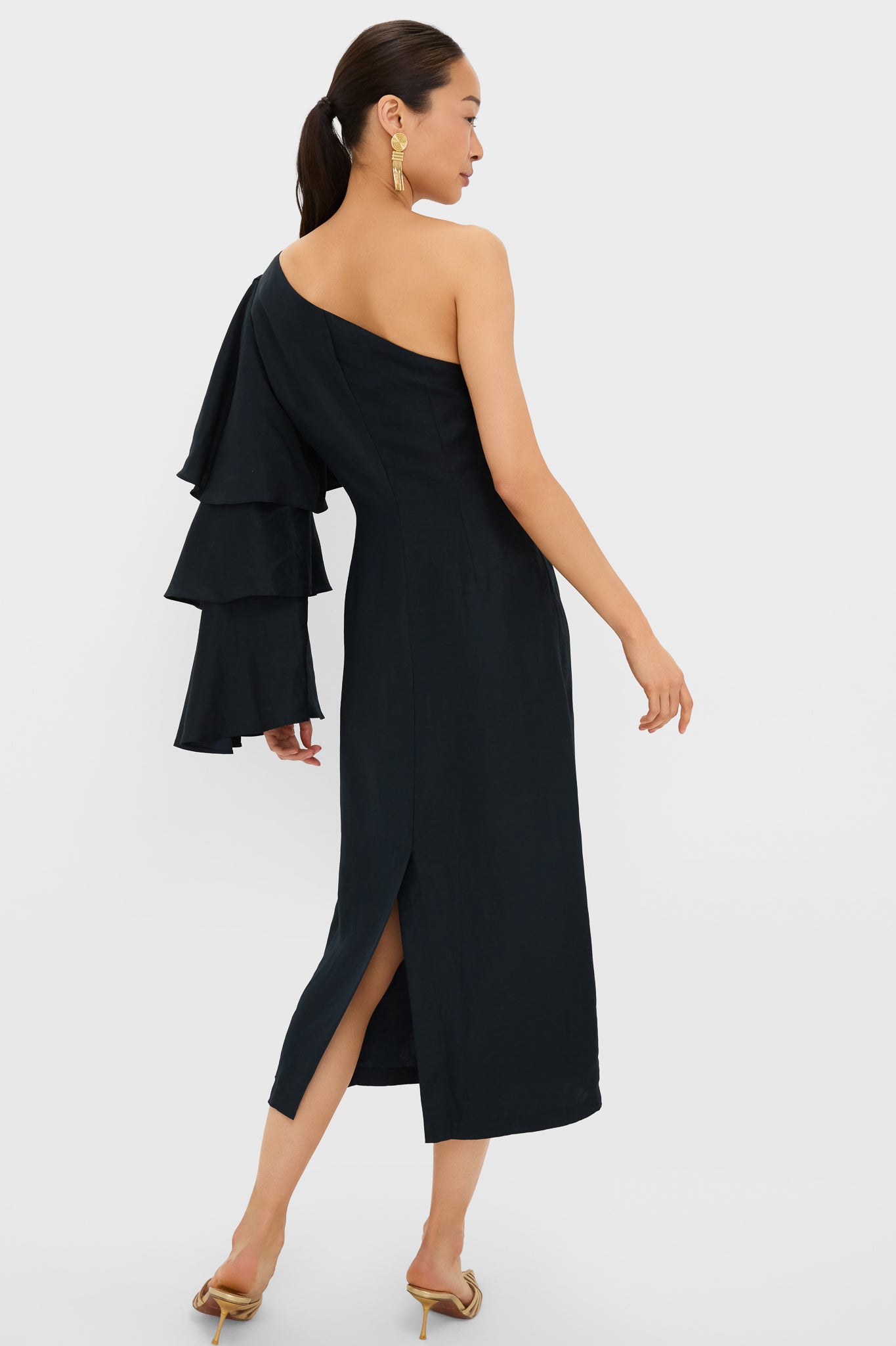 Model in the Black Bidi Bidi Bom Bom Tea Length Dress featuring an asymmetrical neckline, dramatic ruffle sleeve, and back slit, embodying effortless, high-end style for classic, fun occasions.