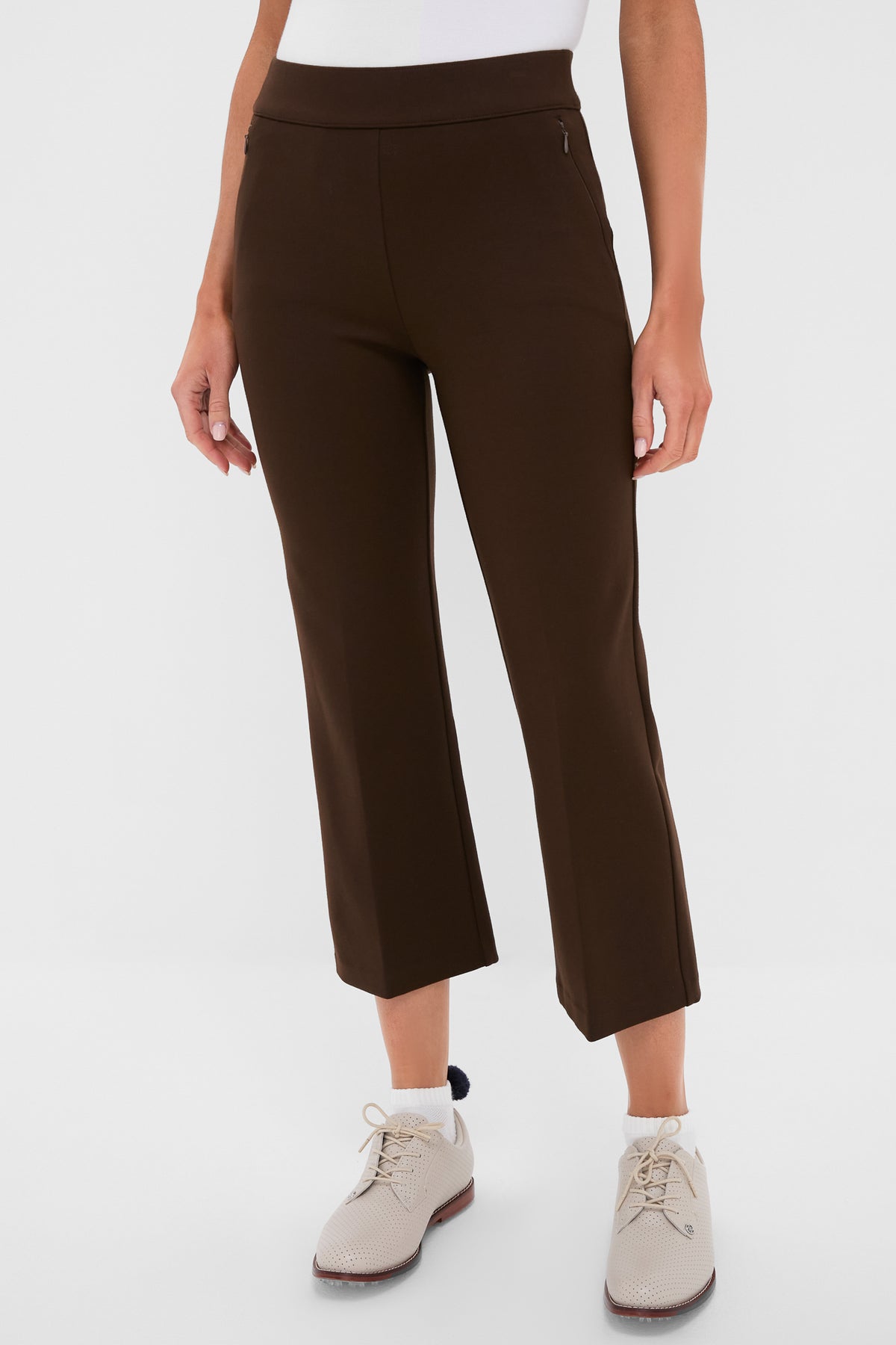 A person stands confidently in Tnuck Sport elevated cropped pants with an elastic waist, a white top, and light-colored lace-up shoes.
