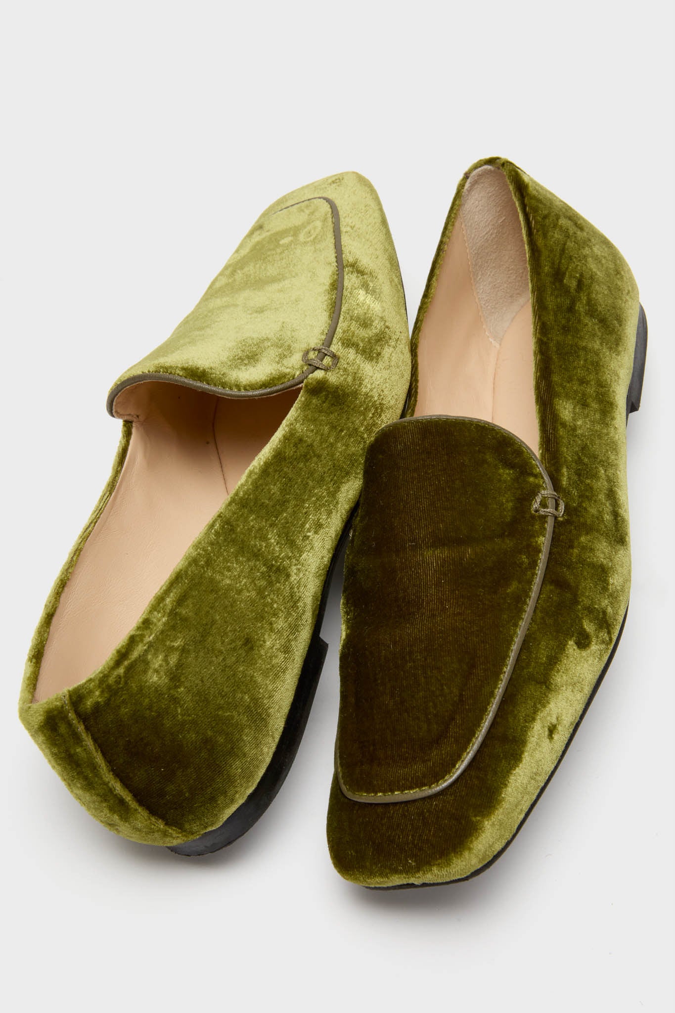 A pair of green velvet loafers featuring black soles and refined leather trim.