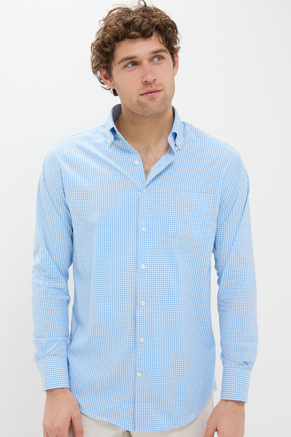 A man wears a Peter Millar long-sleeve button-up shirt in light blue and white check print, made from performance cotton.