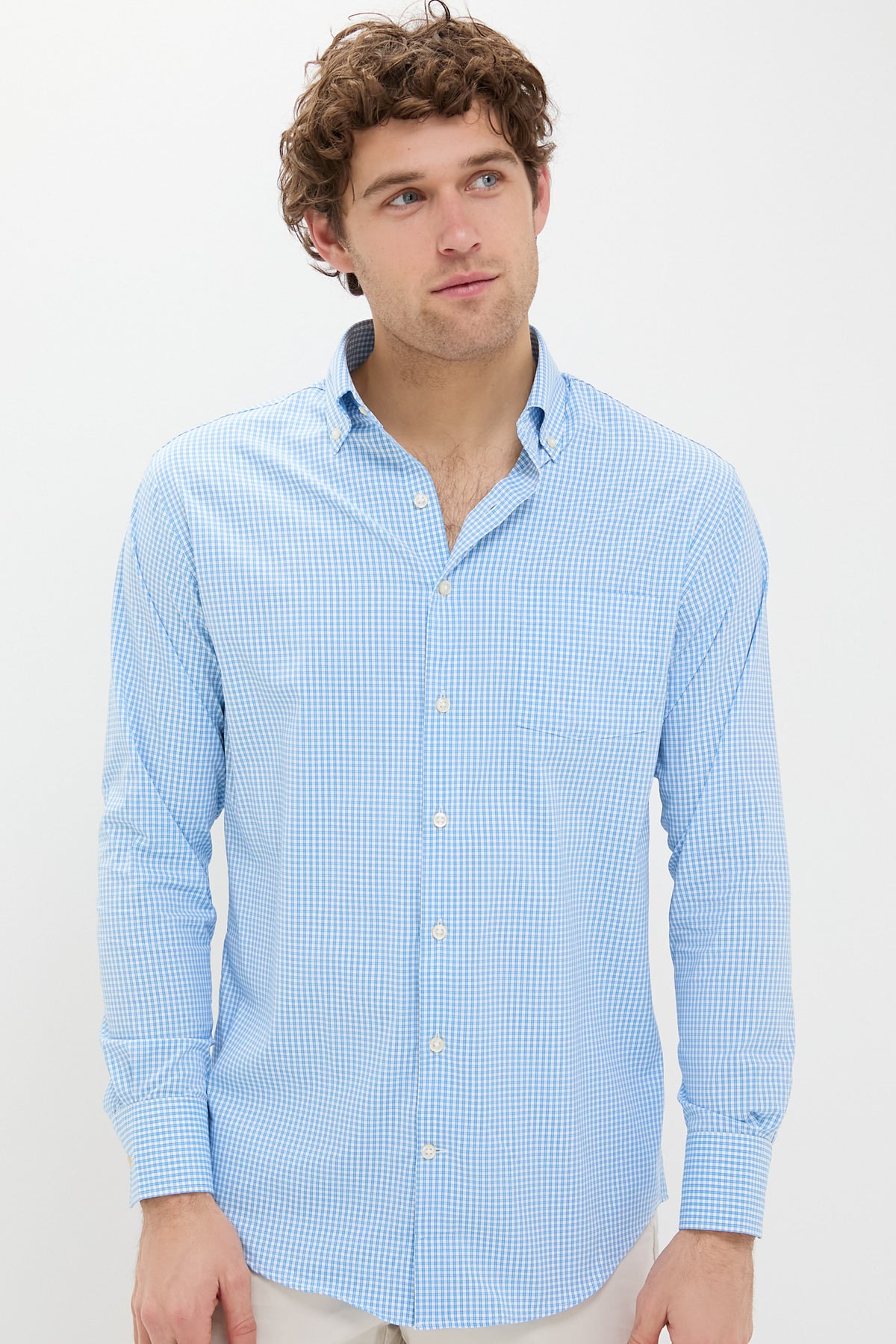 A man wears a Peter Millar long-sleeve button-up shirt in light blue and white check print, made from performance cotton.