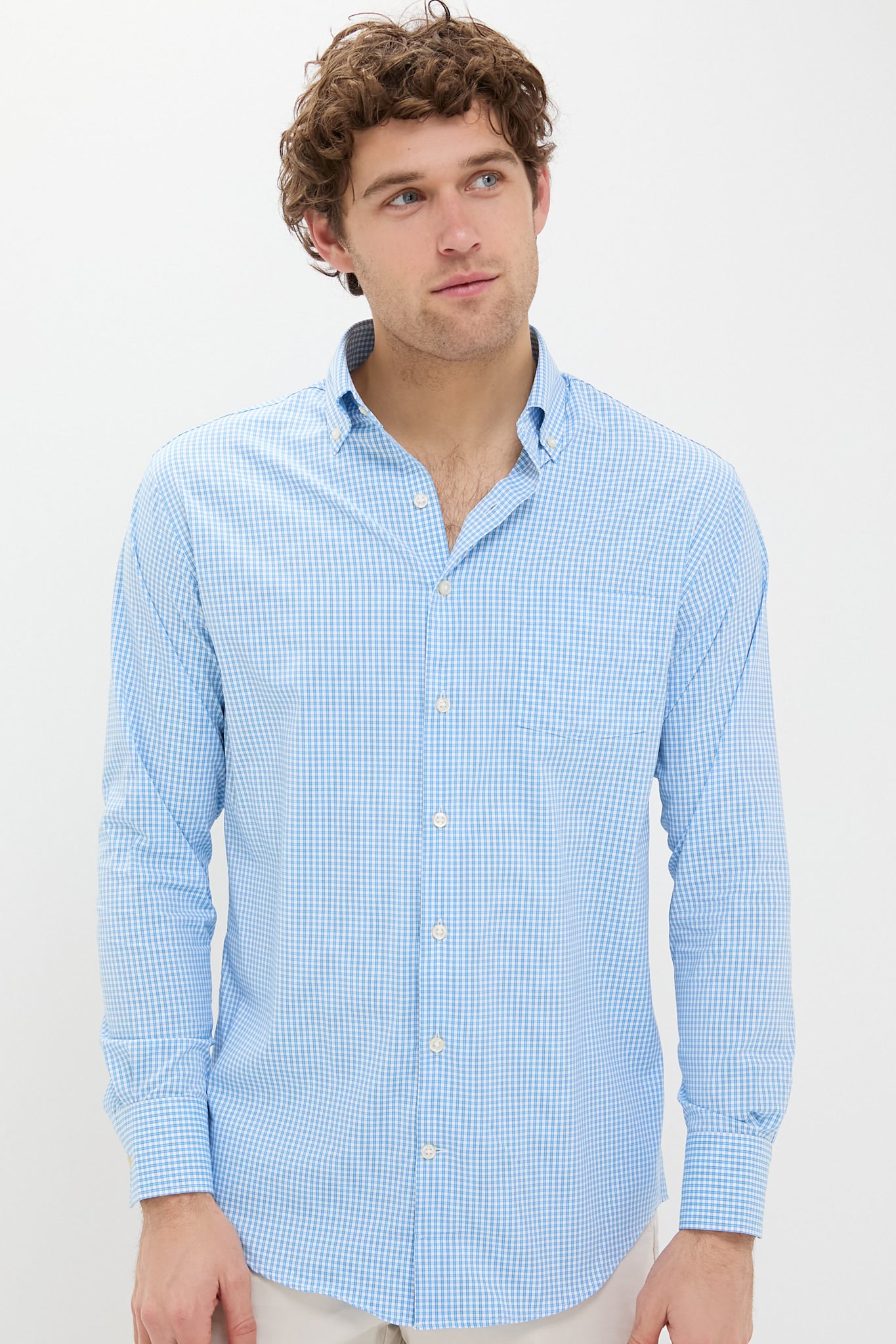 A man wears a Peter Millar long-sleeve button-up shirt in light blue and white check print, made from performance cotton.
