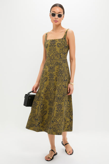 Model wearing the classic Olive Flora Natali Dress, featuring an effortless olive-green botanical print. Accessorized with high-end gold jewelry, sunglasses, and a fun woven handbag.