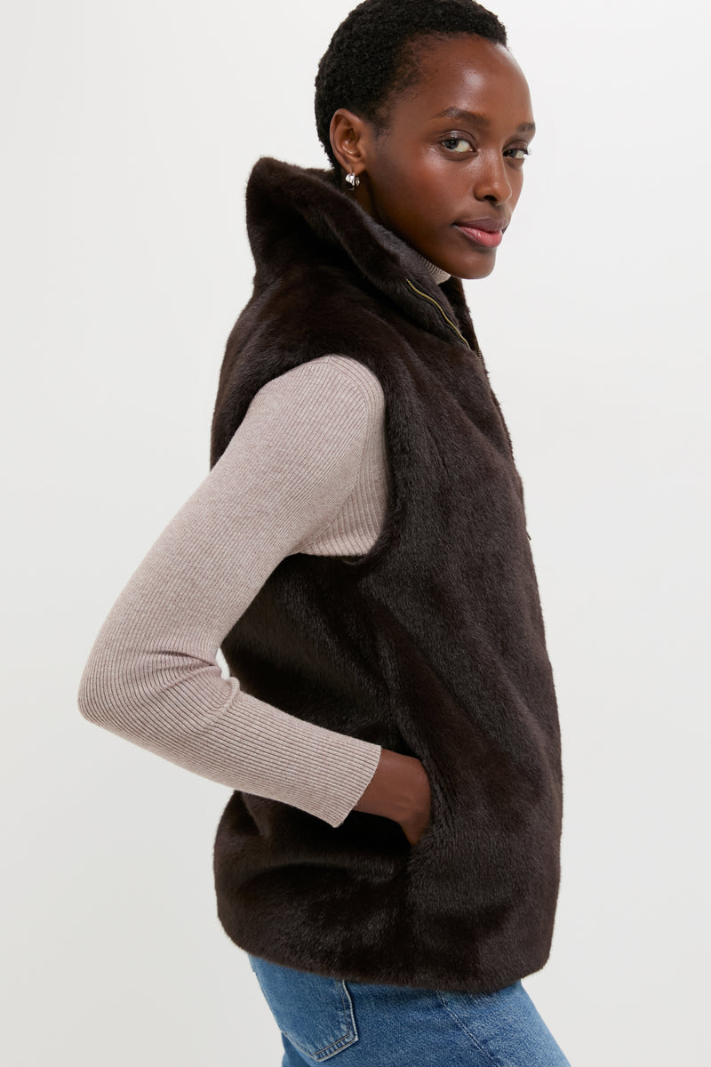 A woman models a Vanessa Bruno Brun Furo Fur Vest over a beige ribbed long-sleeve shirt and blue jeans, posing with one hand in the vest pocket against a plain background.