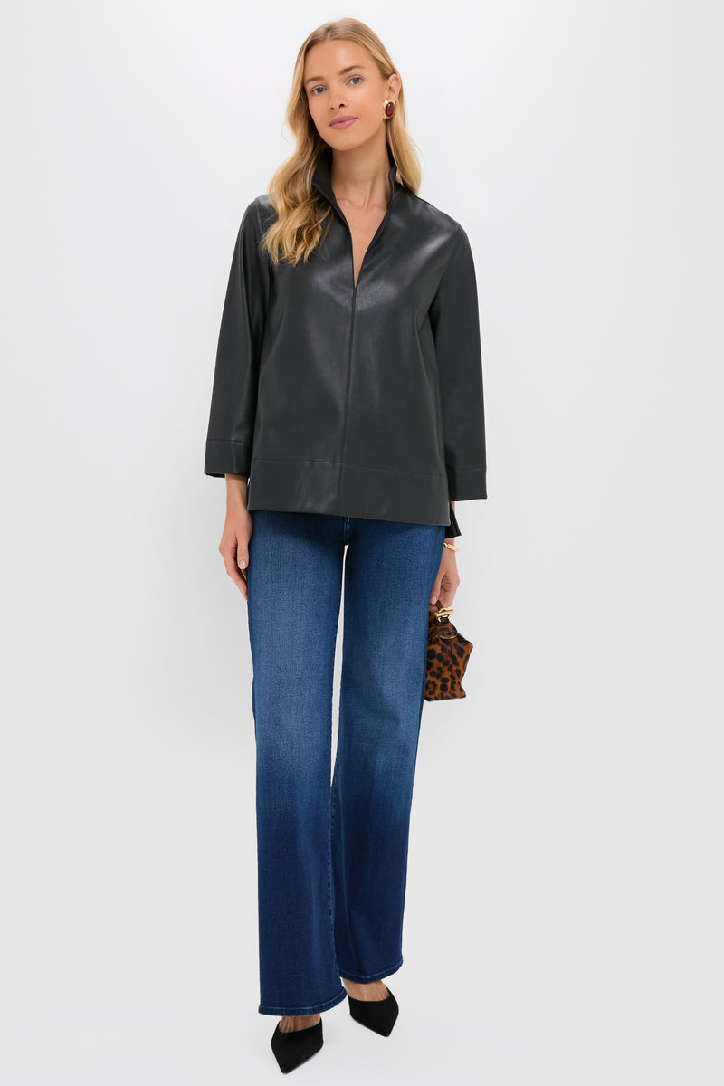 A woman faces forward wearing a Tuckernuck black faux leather blouse, blue wide-leg jeans, black heels, and holding a small animal print clutch.