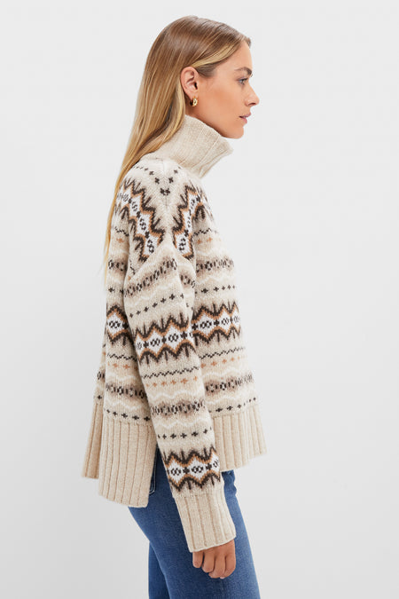 A woman in a beige wool-blend jumper with a brown and black geometric pattern, styled with blue jeans.