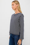 A woman showcases Parisian-chic style in an Alex Mill navy and white striped long sleeve boat neck tee with blue jeans, set against a plain white background.