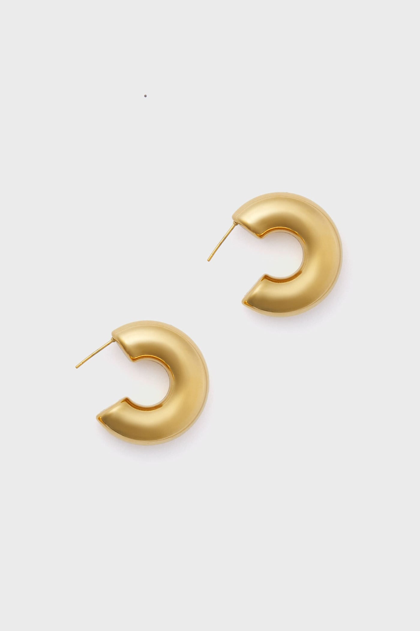 A pair of Gold Leonardo Earrings—crescent-shaped statement hoops with straight posts—from Petit Moments, a female-owned brand.