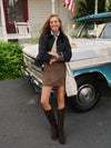 Young woman in a classic, high-end Noir and Noisette Mimi Mini Skirt, effortlessly styled with knee-high boots, leaning against a vintage truck with a fun smile.