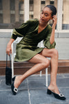 Young woman in olive dress showcasing classic Black Suede Tilda Mules with crystal buckles, embodying an effortless, high-end style for versatile, fun fashion.