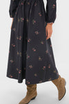 A person wearing the Louise Eloise Midi Dress—a long-sleeved, dark floral print dress—paired with knee-high tan suede boots.