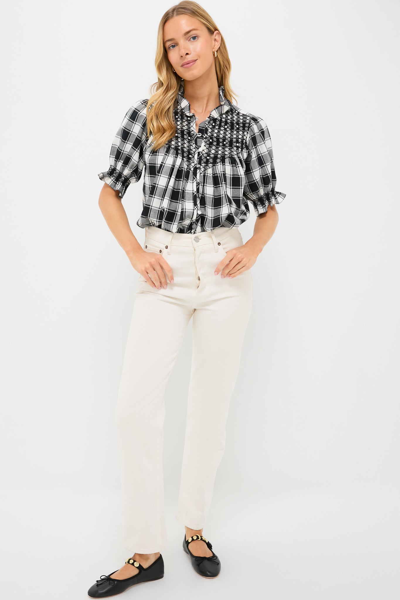 A woman in a Loretta Caponi embroidered flannel blouse with ruffles, paired with white high-waisted pants and black flats, stands against a plain white background.