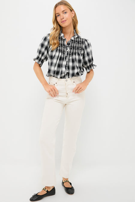 A woman in a Loretta Caponi embroidered flannel blouse with ruffles, paired with white high-waisted pants and black flats, stands against a plain white background.