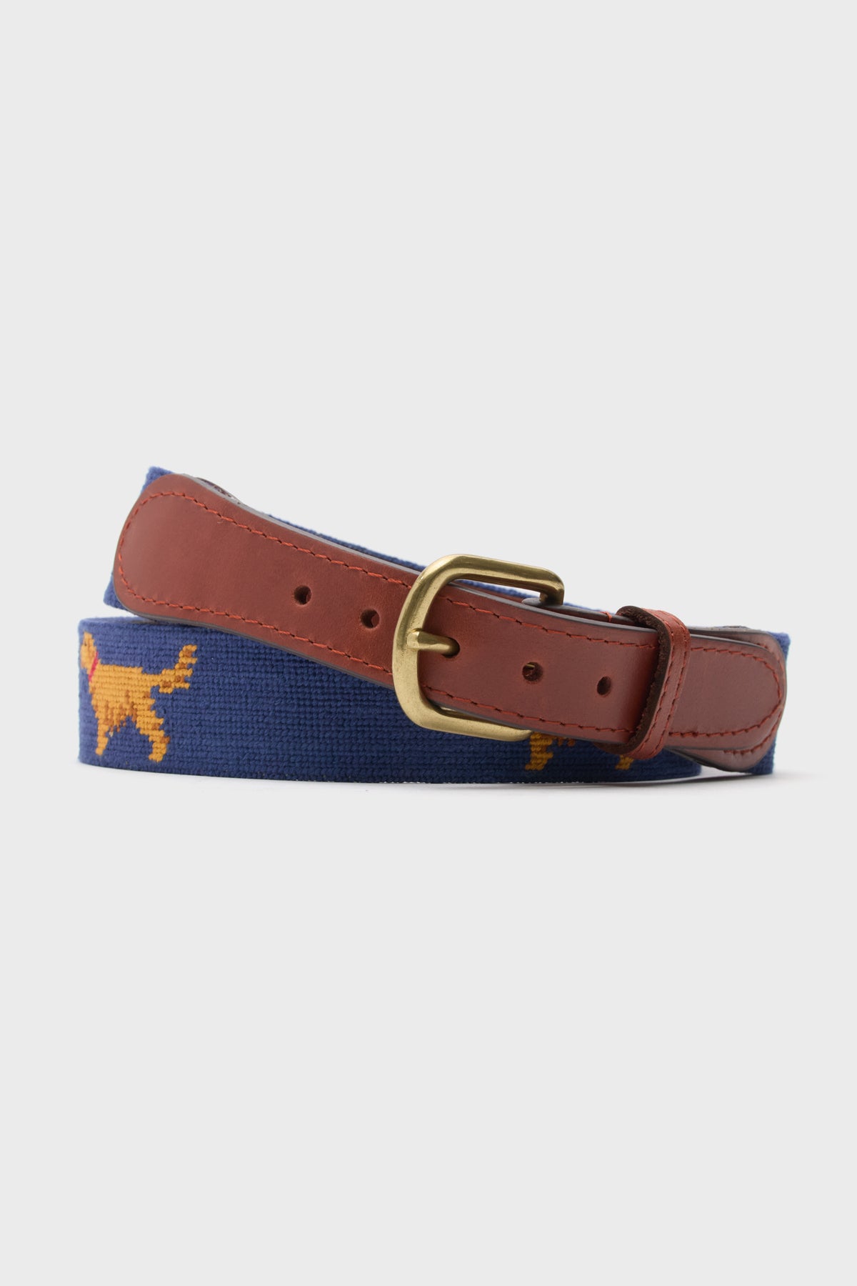 A blue adjustable Smathers and Branson belt featuring hand-stitched needlepoint golden retrievers, brown leather ends, and a brass buckle.