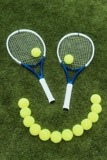 A smiley face made with tennis balls and two tennis rackets. 