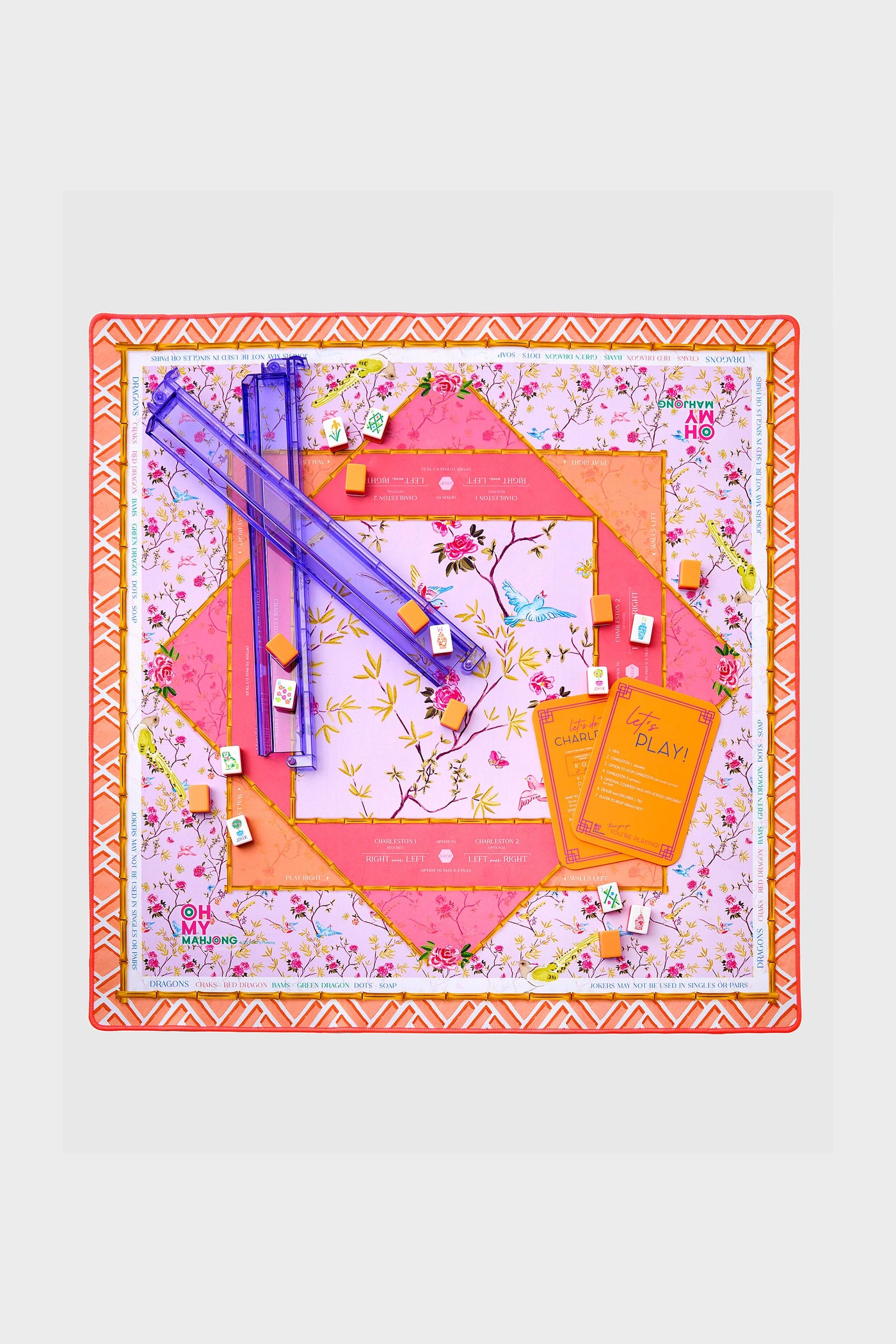 Goldie Playing Mat setup: vibrant, floral Mahjong-style board game with clear purple racks, white tiles, orange markers, and instruction cards for effortless, fun gameplay.