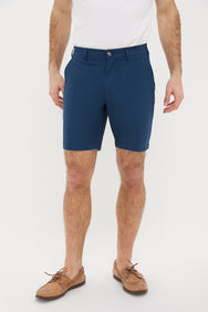 A man stands confidently in a white t-shirt, brown boat shoes, and blue stretch shorts by Peter Millar.