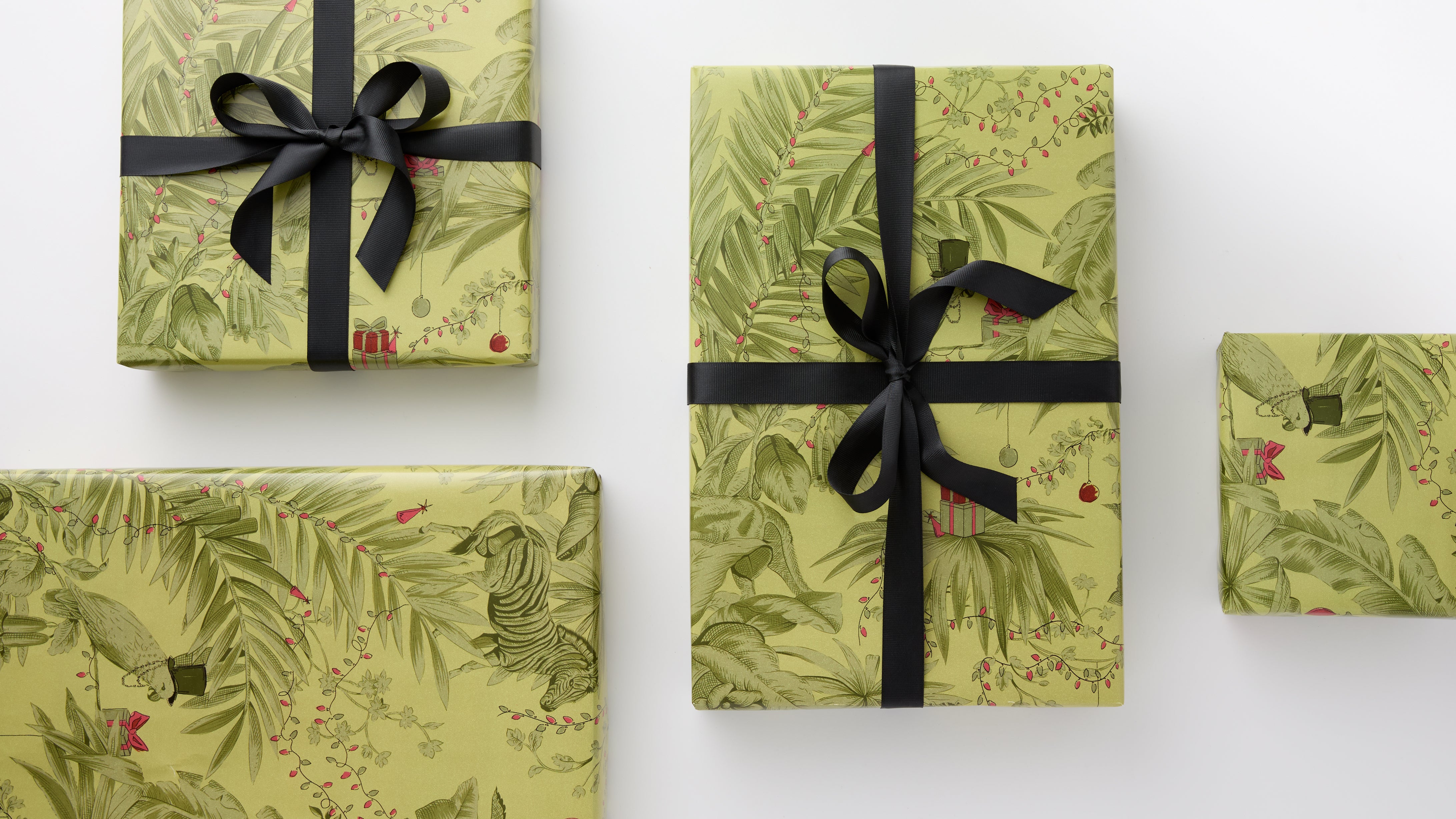 Gift Wrap: Four elegantly wrapped boxes in pale green with botanical motifs and whimsical animals, tied with black satin bows offer an effortless, fun, and high-end presentation.